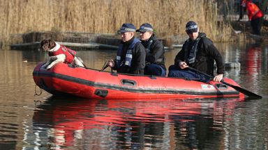 Police in a RIB with a sniffer dog search a pond on the common